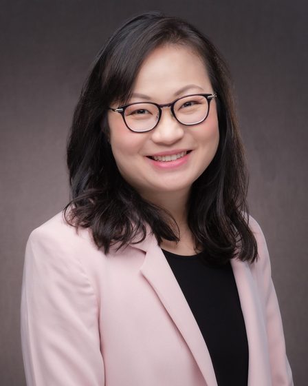 Dr Audrey Pang in a pale pink jacket, facing the camera against a plain studio backdrop.