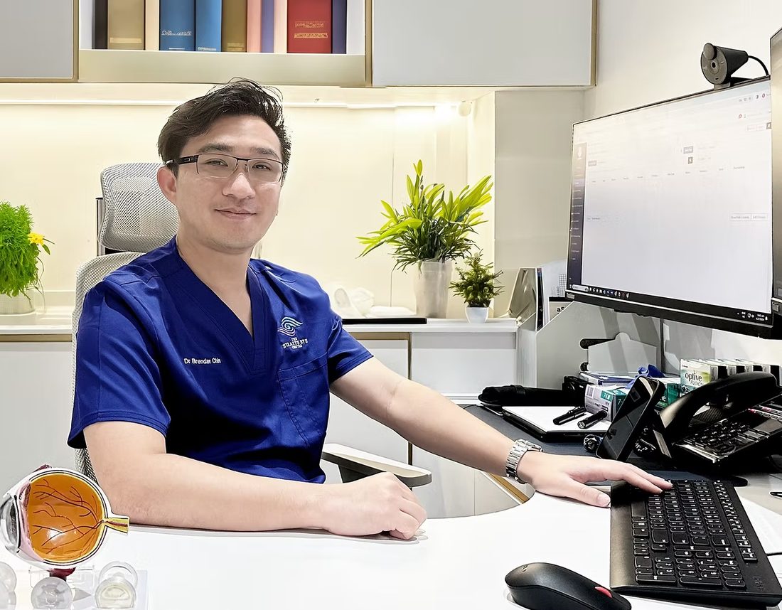 Dr Brendan Chin seated at a consultation desk beside a monitor in the clinic.