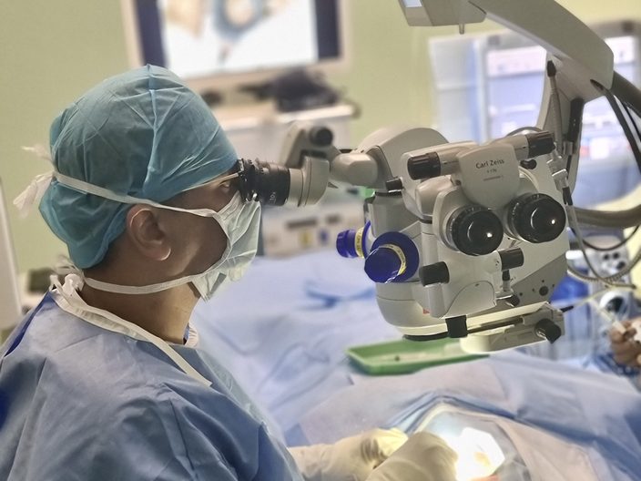 Dr Jayant V Iyer operating at a microscope in an operating theatre.
