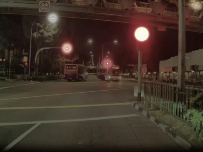 A driver&rsquo;s view of a road at night, the traffic lights and a street lamp each surrounded by a soft ring of glow.