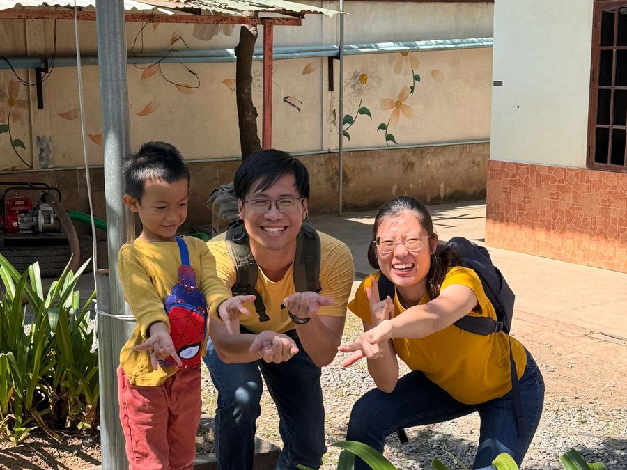 Dr Seow crouching between a colleague and a young boy in a courtyard, all three smiling at the camera.
